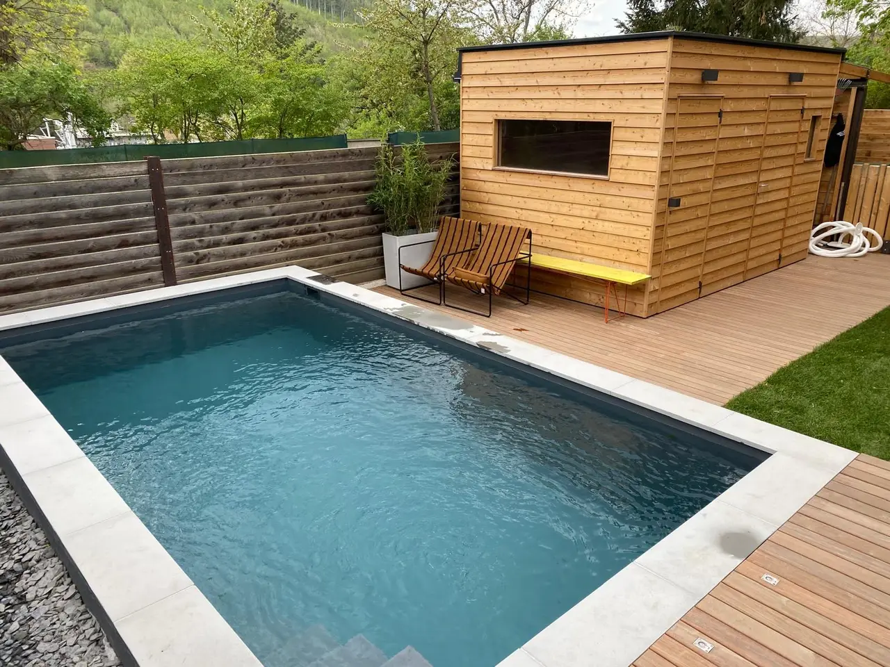 Schwimmbecken mit Natursteinkante und Poolhaus aus Holz