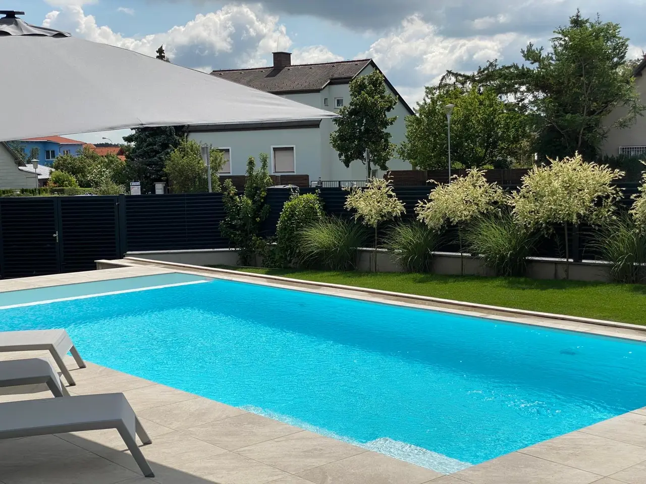 Rechteckpool mit Steinumrandung und Sonnenliegen
